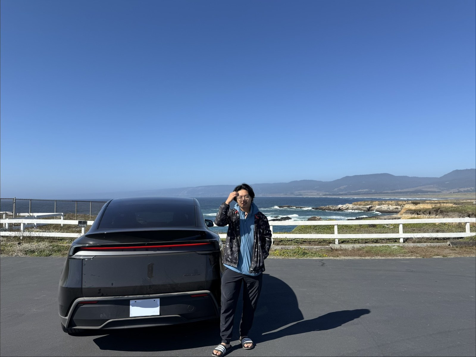 人和车停在白围栏边,海崖在身后