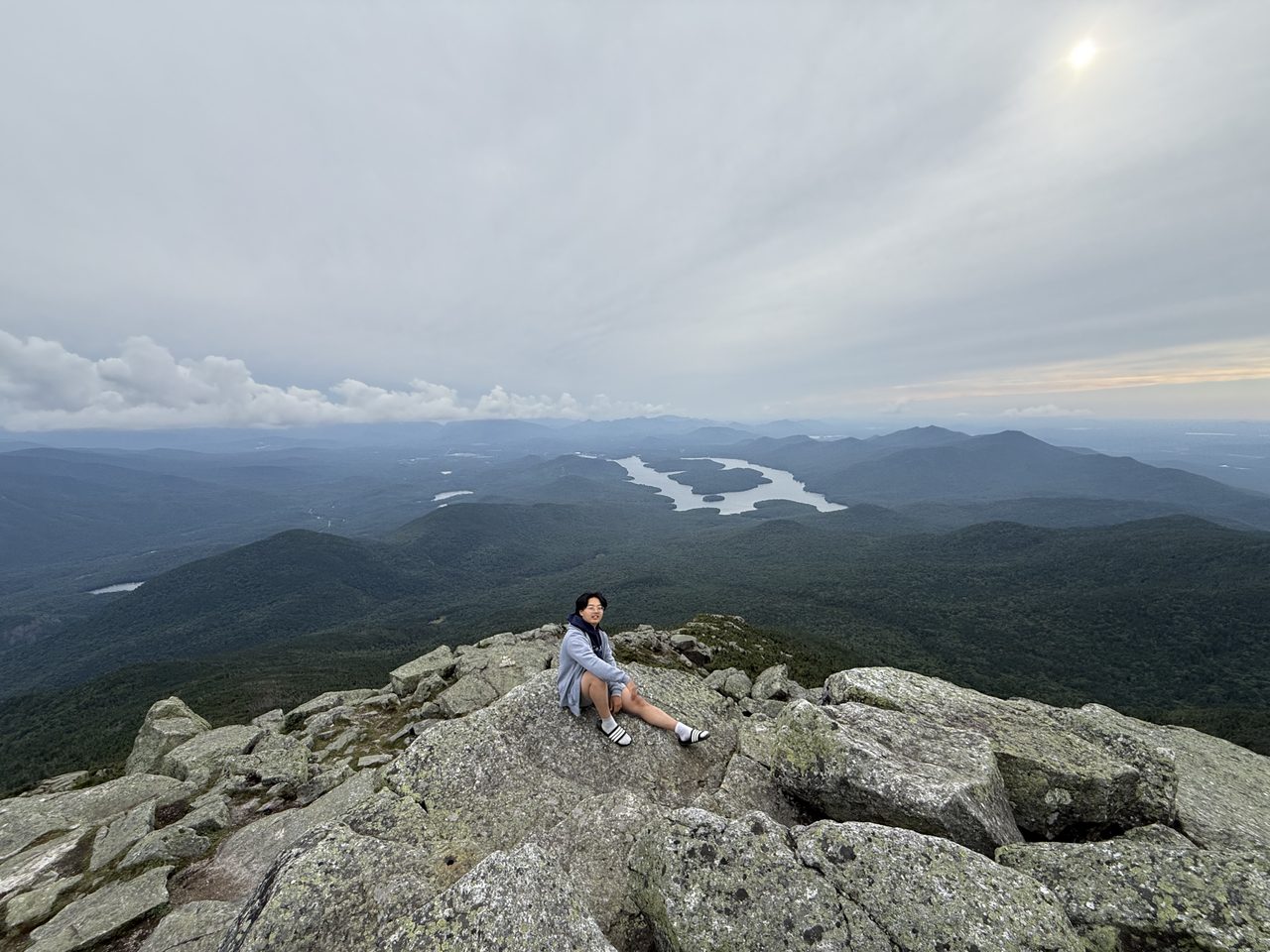 一人坐在山顶浅色巨石上，身后是远处的普莱西德湖和群山