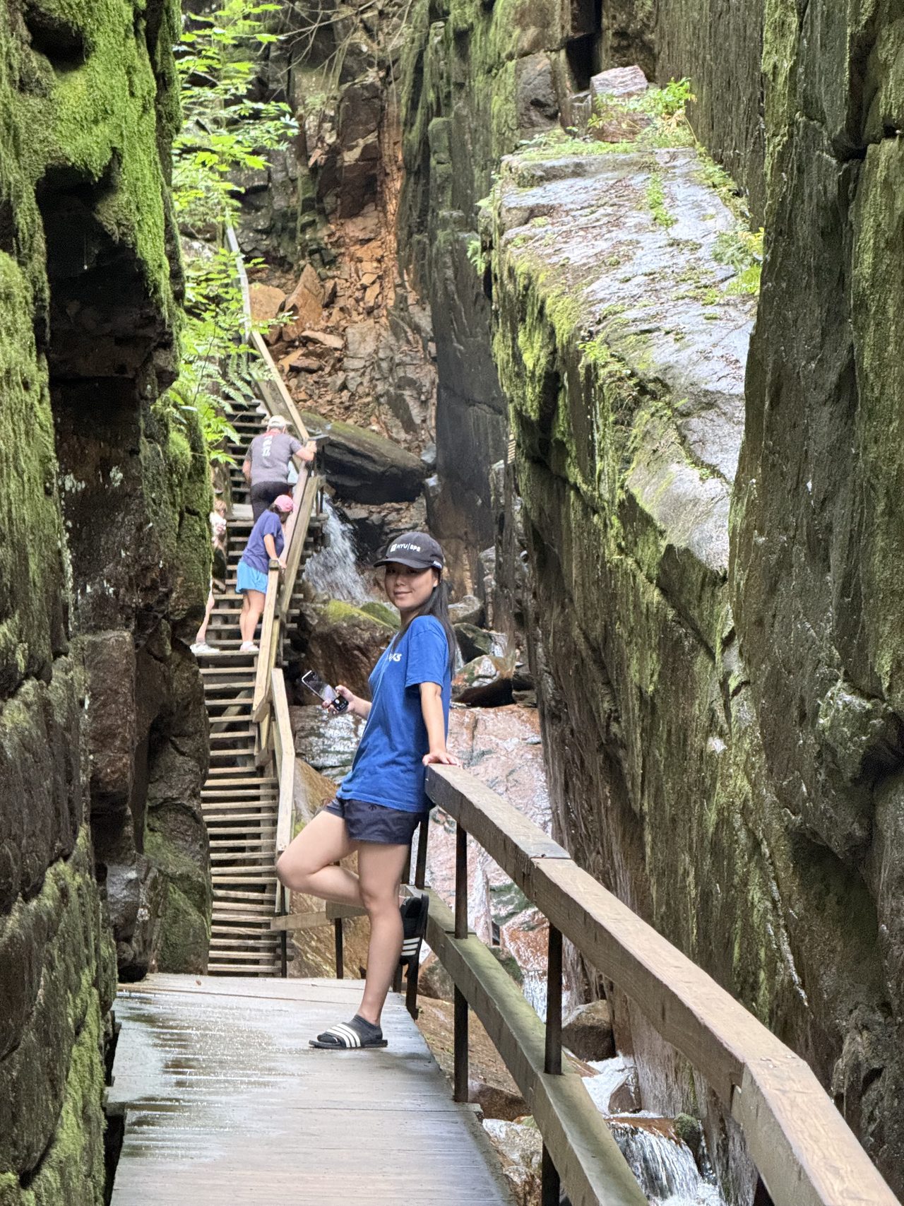 A person on a boardwalk between tall moss-covered granite walls in a narrow gorge.