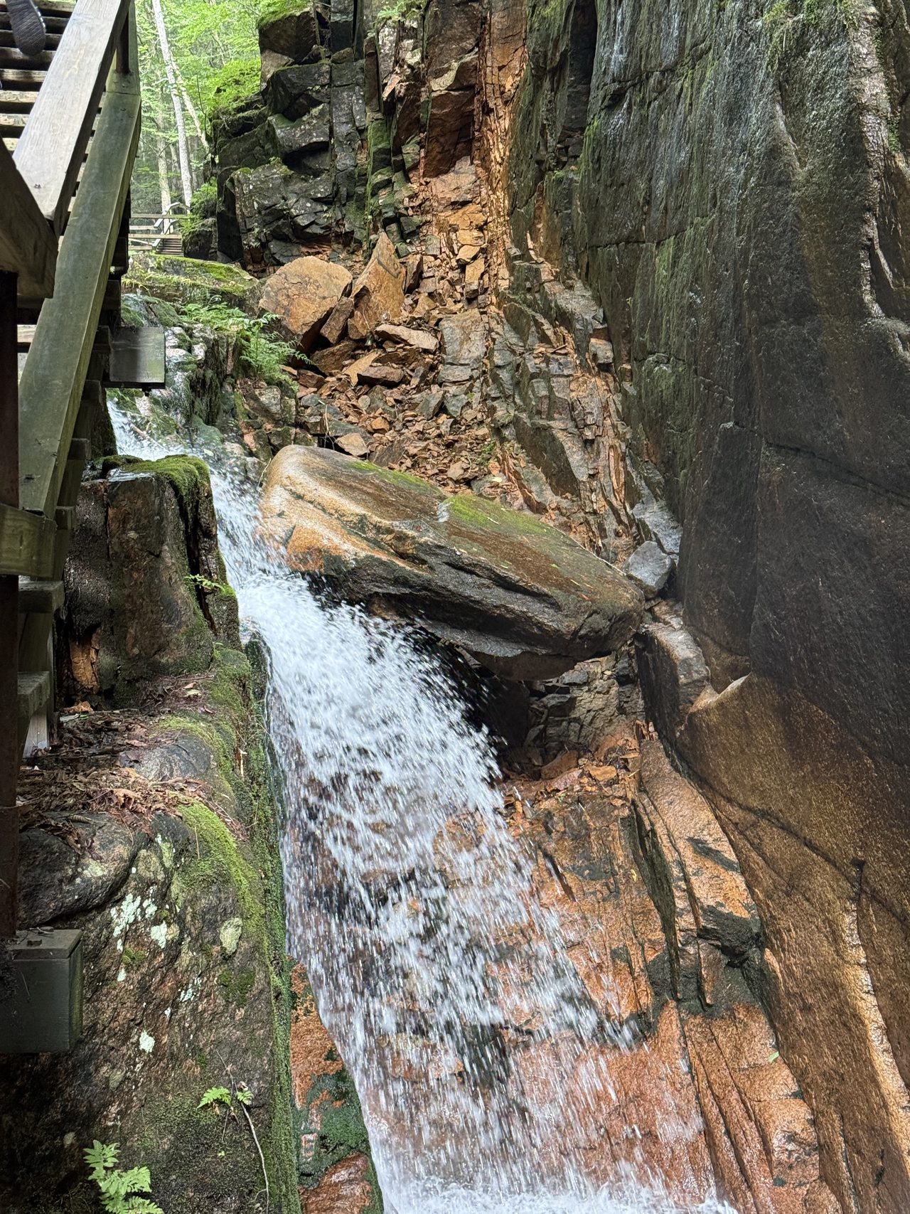 A waterfall cascading down granite beside wooden boardwalk stairs in a gorge.