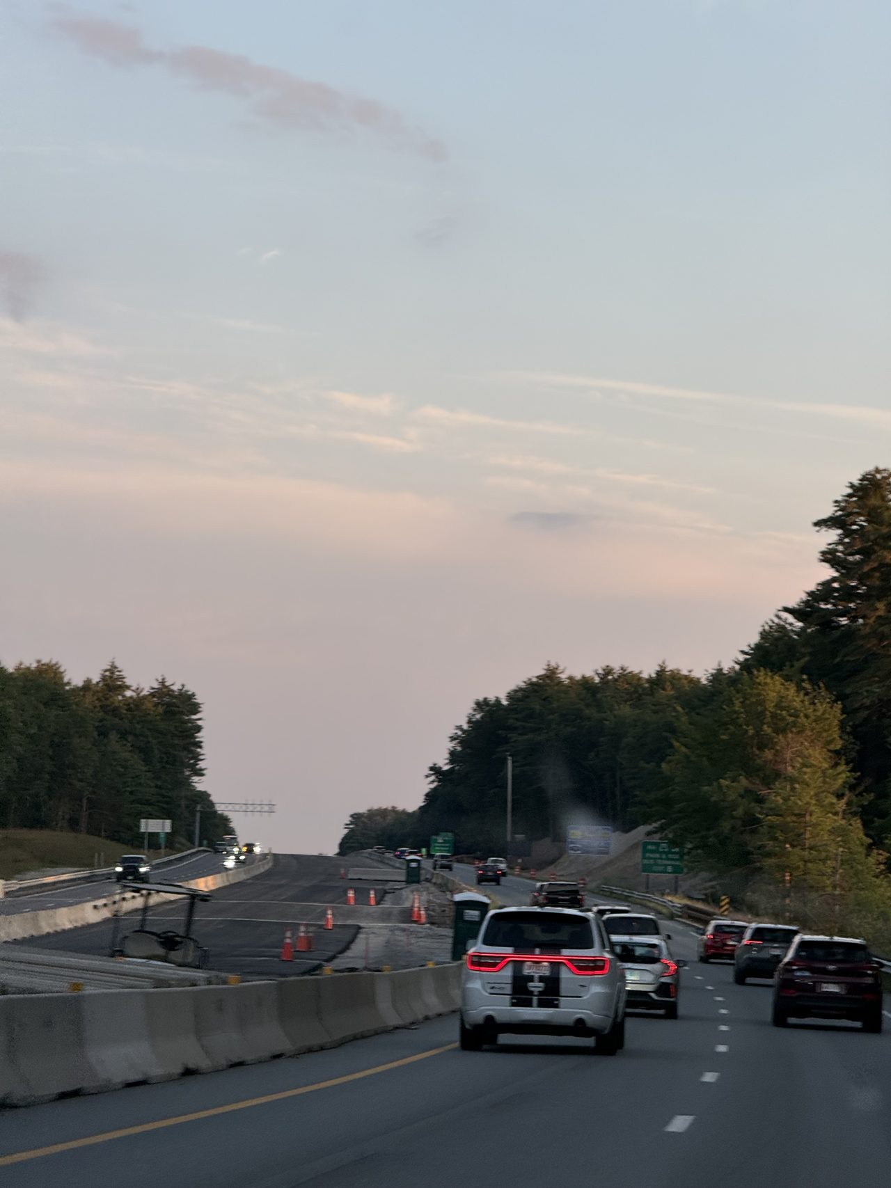 Evening highway traffic beside a coned-off construction zone under a pastel sky.