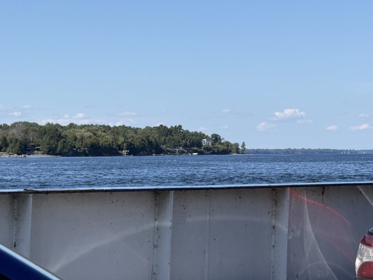 A ferry deck with an orange life ring, passengers at the rail and open lake beyond.