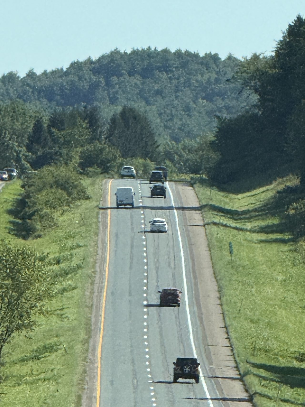 A divided highway with green exit signs and light traffic among trees.