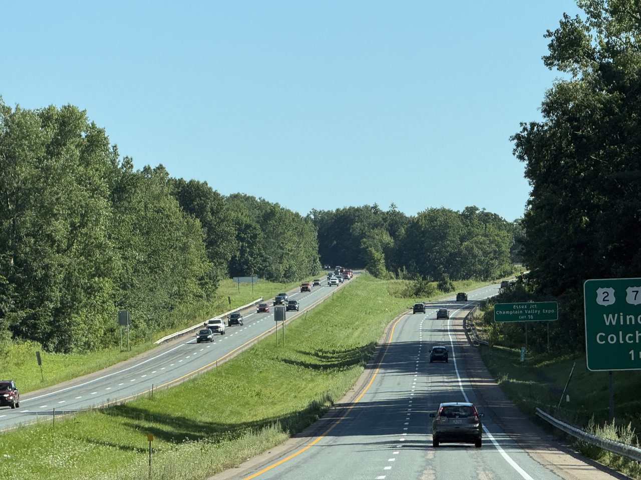 A highway curving toward layered green mountain ridges under a blue sky.