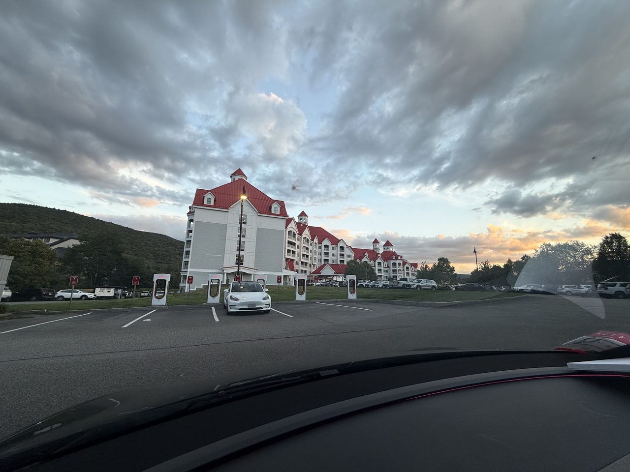 Tesla Superchargers in front of a large white resort building with red roofs at dusk.