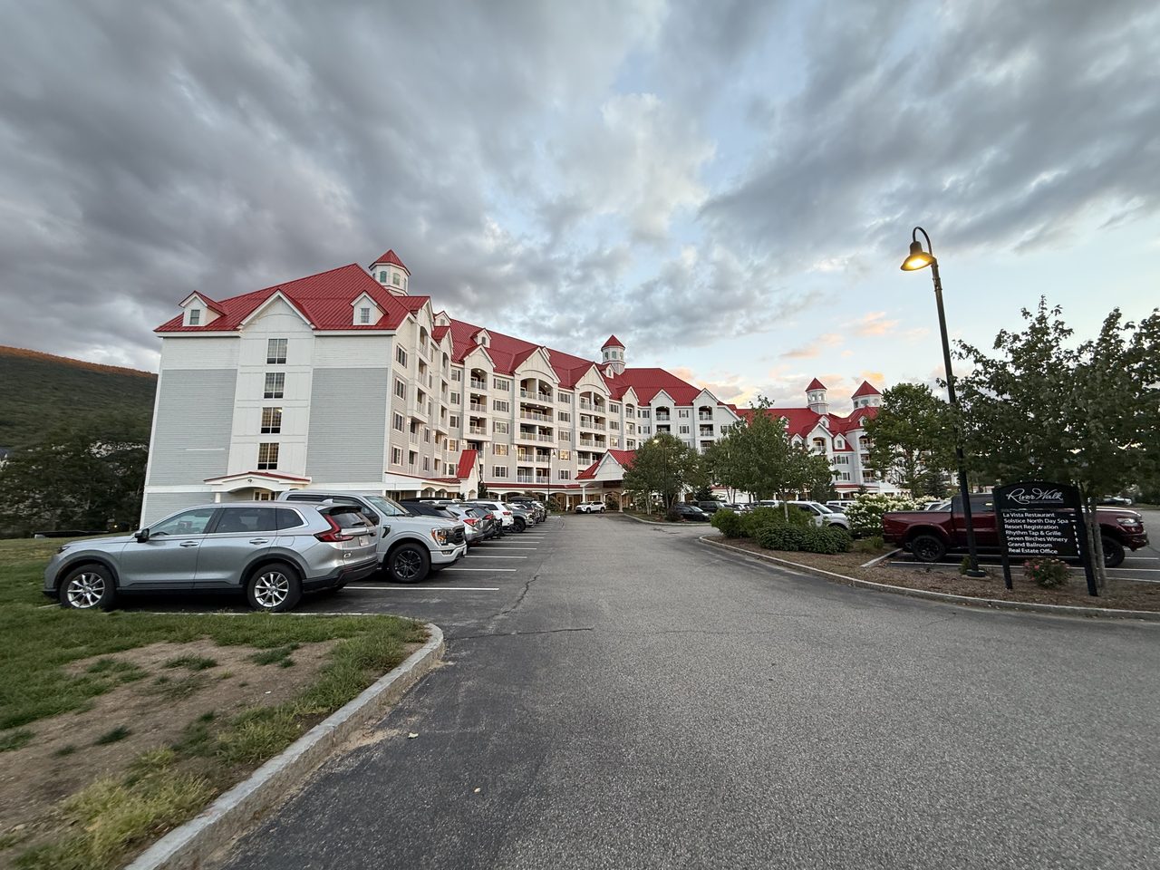 A large resort with red roofs under dramatic dusk clouds, cars in the lot.