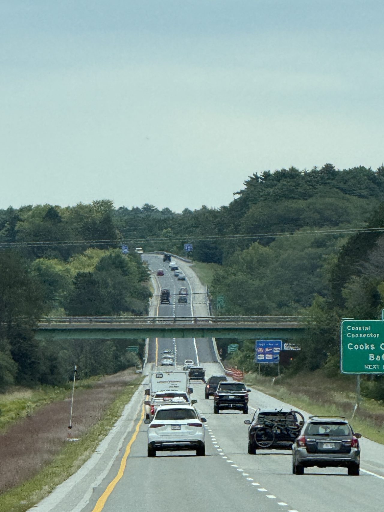 A highway descending toward an overpass with green destination signs.