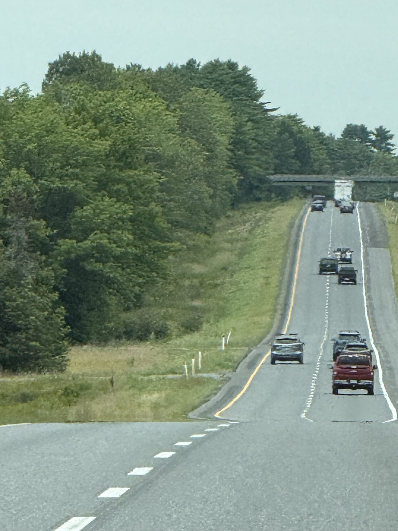 A rolling tree-lined highway with light traffic under a hazy sky.