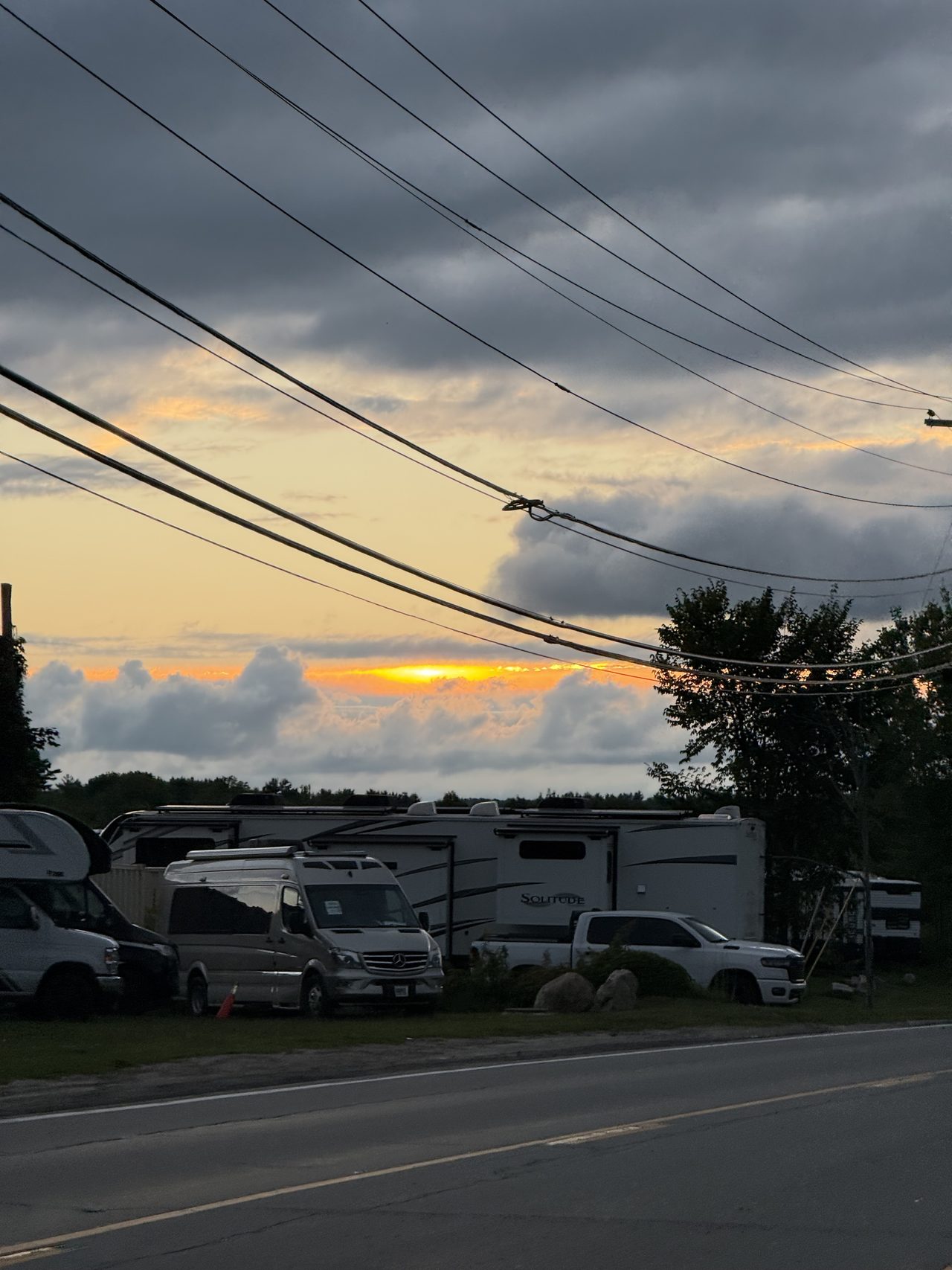 A vivid orange sunset visible through a gap between cloud layers above parked RVs.
