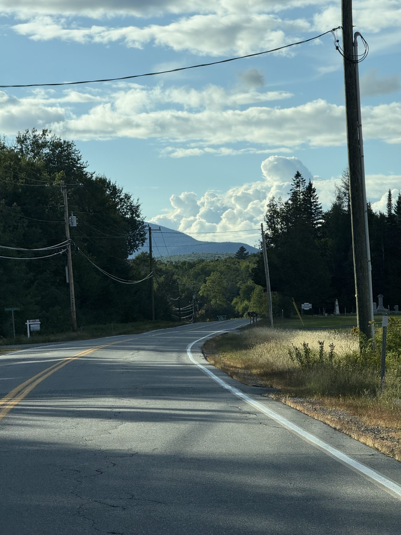 A rural road with utility poles leading toward a rounded forested mountain.