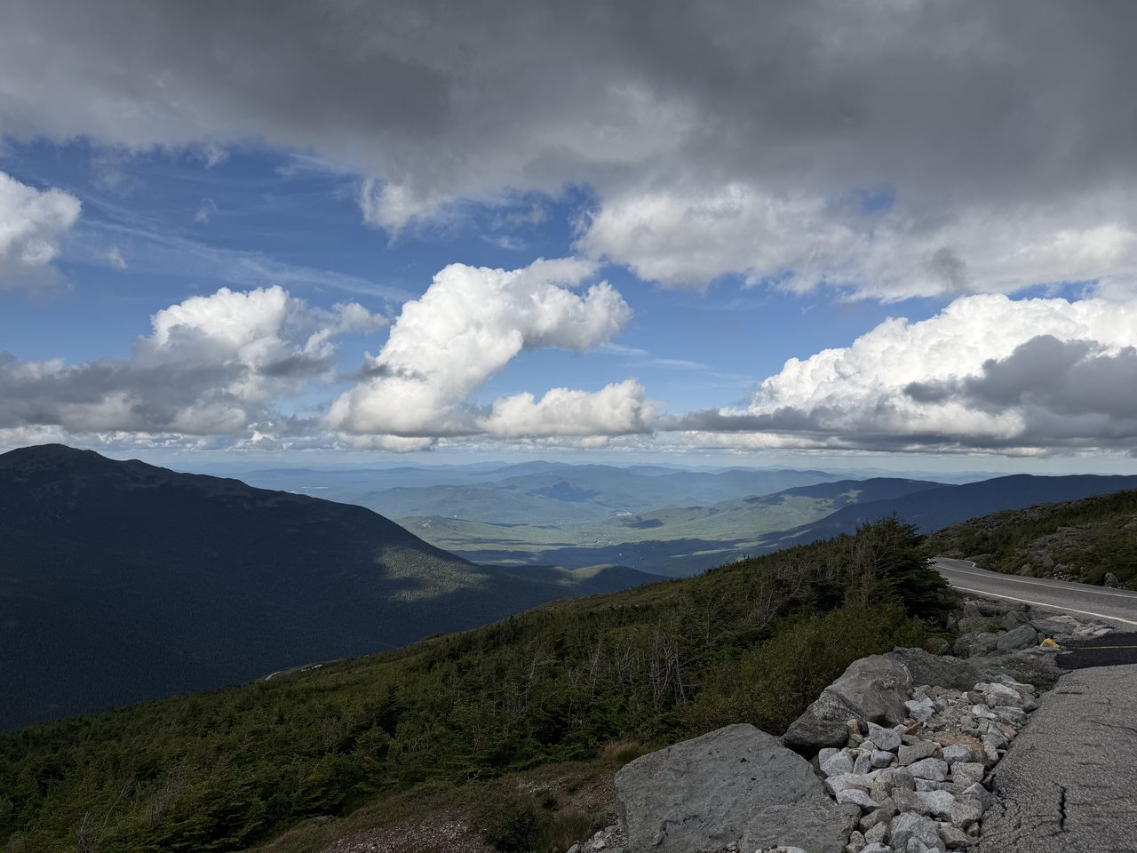 A view from a mountain road over deep green valleys and blue ridges under big clouds.