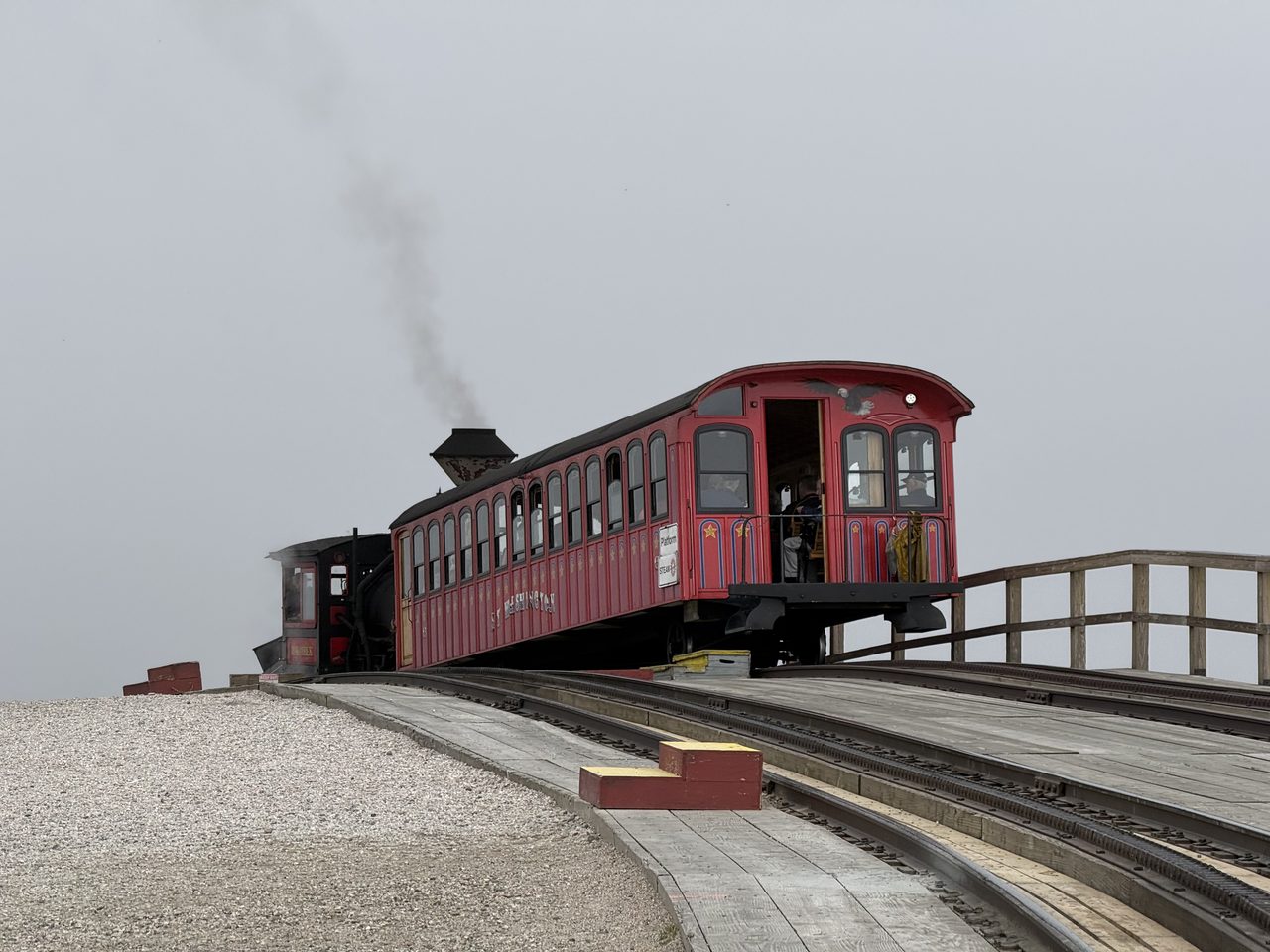 A red vintage railway carriage on a steep cog railway track emerging from thick fog.