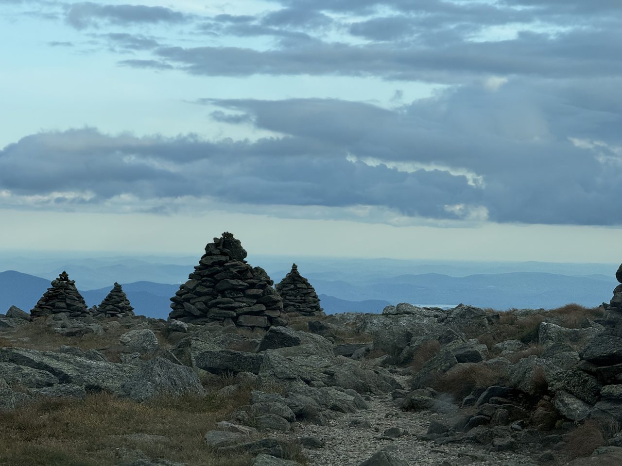 Several stone cairns on a rocky alpine plateau under a dim evening sky.
