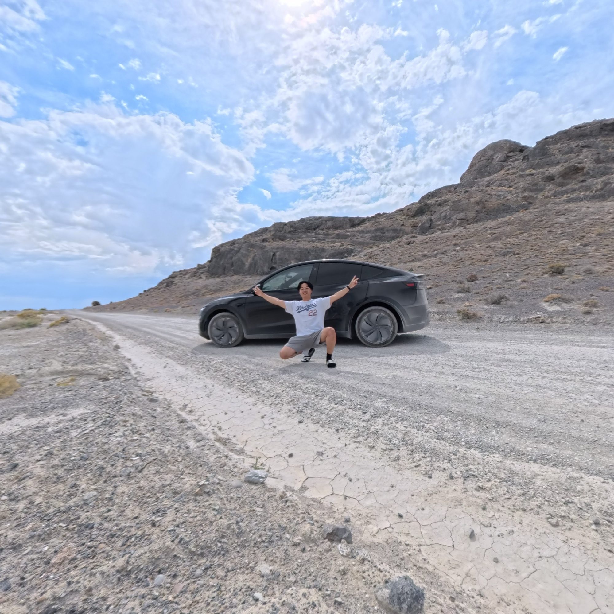 Crouching by the Model Y on a cracked playa road