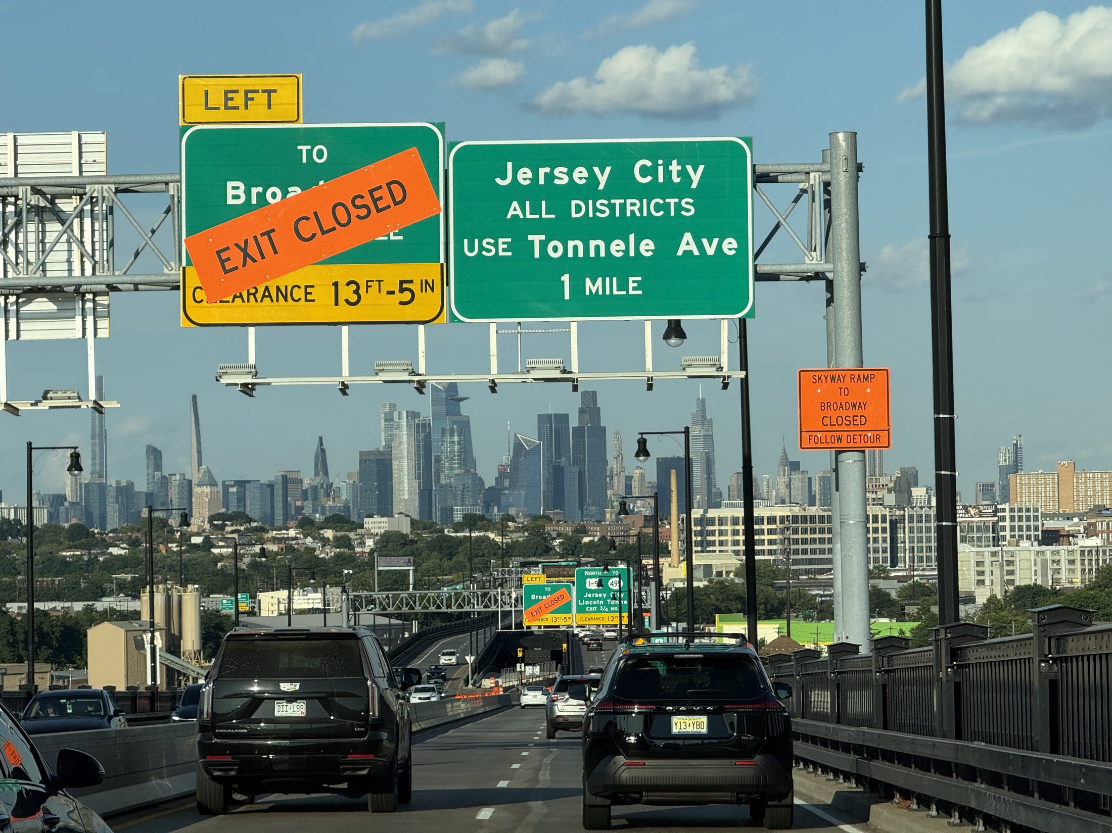 The Jersey City ALL DISTRICTS sign with the Manhattan skyline behind
